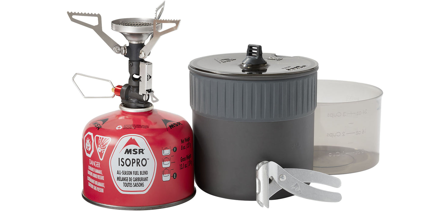 The MSR Pocketrocket delux kit, with the camp stove, isopro propane tank, a cooking pot and a aluminum pot lifter. A small clear measuring cup is also beside.