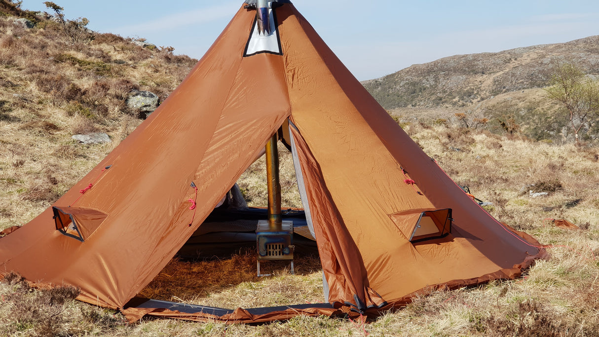 Inside the entry way of the NorTent Iavvo 4 Winter hot tent with a small portable camp furnace in the middle. The furnace chimney is brought through the roof of the teepee formed tent.