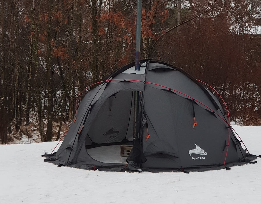 Nortent Gamme 4 Winter Hot Tent in black with red tent poles. The tent is set up outside in the snow amongst a group of trees.