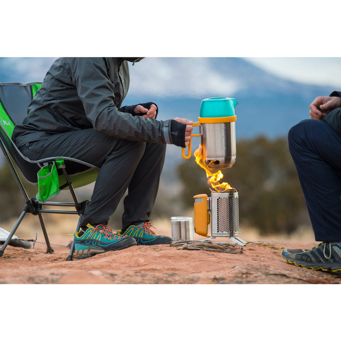 A well dressed canyon hiker pulling off the hot kettle pot from BioLite CampStove 2. Both hikers sitting close to the fire.