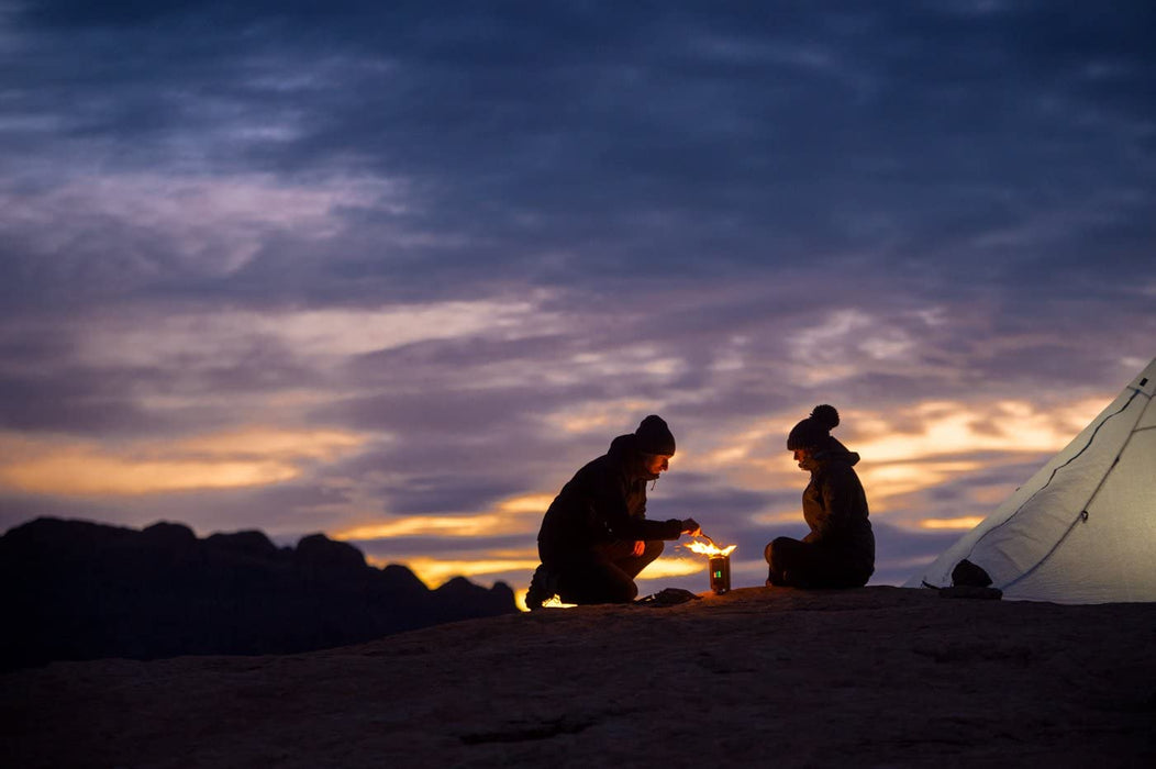 A couple sitting around a fire made by BioLite CampStove 2 at sunset outside of their tent.