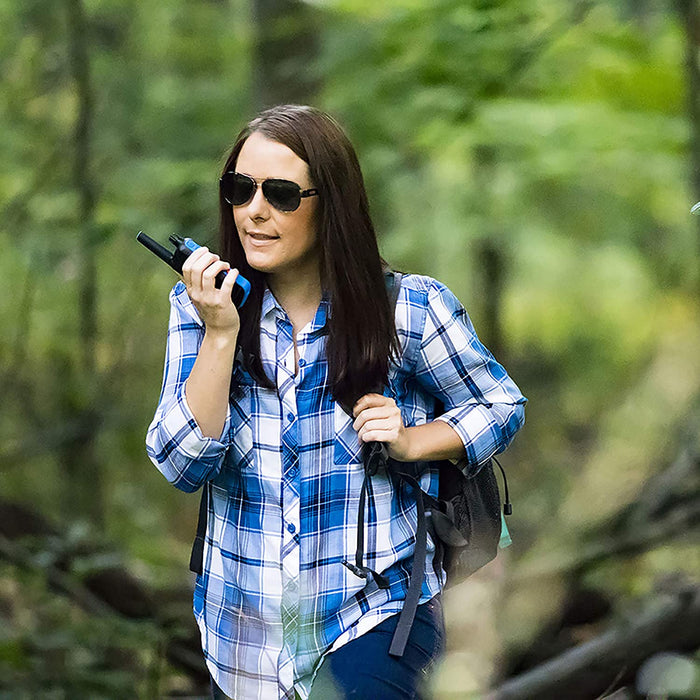 A woman wearing a blue and white plaid shirt speaking into a Motorola T800 two way bluetooth radio in a forest area.