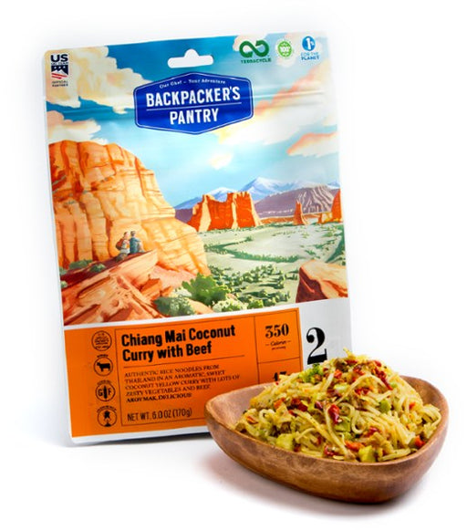 Freeze dried package of backpackers pantry chiang mai coconut curry with beef, along side a wooden bowl of the prepared meal