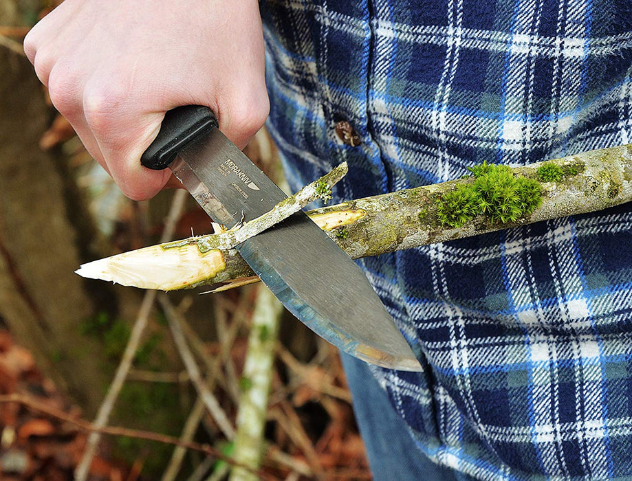 A man wearing a blue and white plaid shirt widdling a stick wtih moss growing on it with a Morakniv Pathfinder Knife.