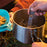 A person scooping noodles out of a camping pot with a UCO titanium spork. A person wearing an orange sweater holds a blue bowl next to the pot.