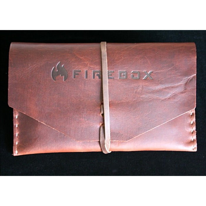 Firebox 5 inch camp stove in a brown leather case with a leather strap holding it together on a black velvet surface.