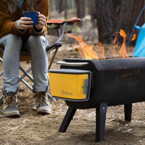 Person enjoying a camp mug beverage, while calmly watching the flames of the BioLite FirePit, out in the wilderness within the trees.