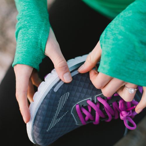 Woman in a kelly green sweater placing Reflective patches on her running shoes
