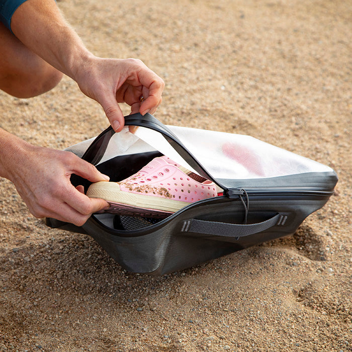 A man putting away pink beach shoes covered with sand into a Nite-ize Waterproof packing cube.