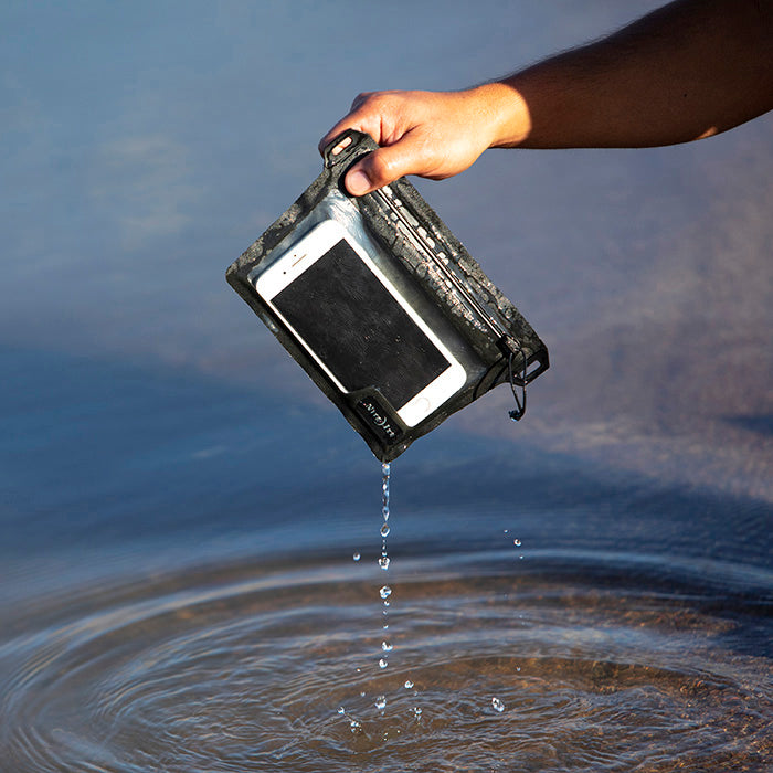 A phone inside a Nite-ize waterproof packing cube wallet case being submerged in lake water.