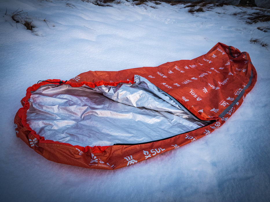 The Escape Pro Bivvy exposing the heat reflective interior on a snowy hillside.