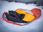 A orange and black sleeping bag stuffed into the Escape Pro Bivvy outdoors on a snowy hillside.