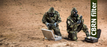 Two men in full Army Camo hazmat suits wearing gasmasks equipped with Mira NBC-77 40mm Thread filters in a desert area with two pelican cases with radiation meters and testing tubes. The description 'CBRN Filter' is shown in a green banner.