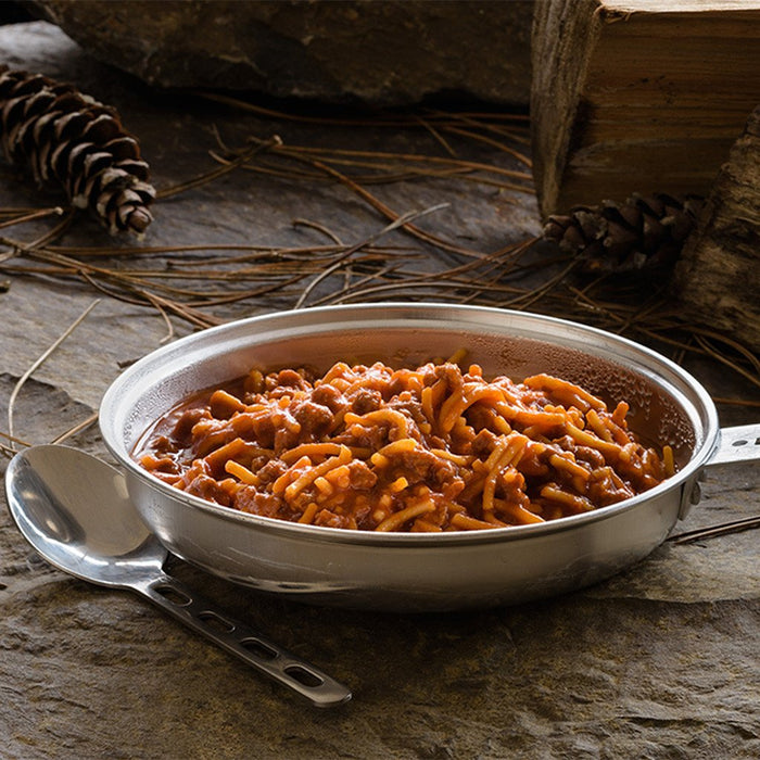 Stainless steel camping pot full of prepared Spaghetti and meat sauce freeze dried food. Surrounding the pot are pine cones and pieces of firewood.