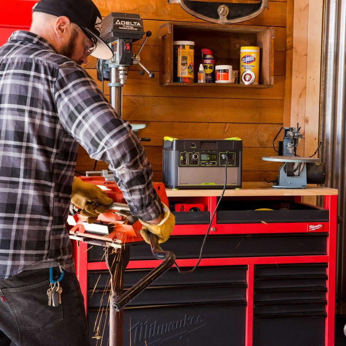 Man using a chop saw to cut pipe powered by a Goal Zero Portable power station. The man is wearing a plaid shirt and safety glasses working in his garage with a milwaukee tool cabinet.