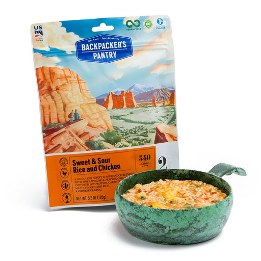 Front cover of Backpackers Pantry sweet and sour chicken with rice and vegetables freeze dried food package. Alongside is a fresh bowl of the prepared product in a camping pot with handle to heat over the fire.