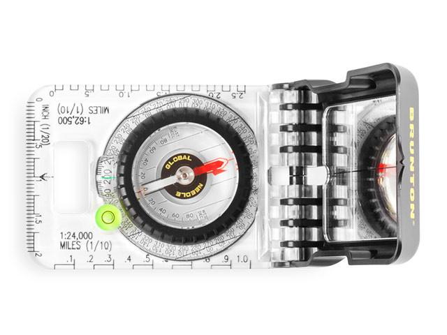 The Brunton TruArc 15 Reference compass laid bottom down on a white background. The dial, degree measurements, ruler with 1:24,000 miles reference, and the mirror are shown. The compass is a clear plastic and the cover is matte black with the brunton logo in yellow.