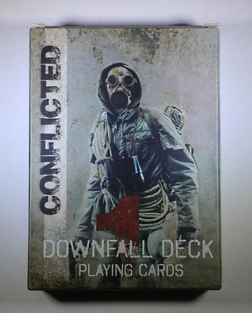 Conflicted Deck 1: The Downfall playing cards. A person wearing a forest green jacket a with gas mask on, binoculars around the neck and rope around wrapped the body poses on the front of the card deck.. 