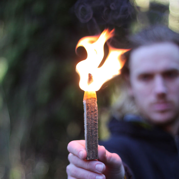 A faded view of a man holding a Behemoth stormproof match, the match is lit and flaming.