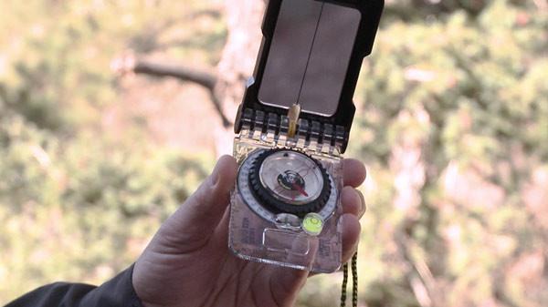 Person holding the The Brunton TruArc 15 compass in their hand with tree's and sunlight in the background.